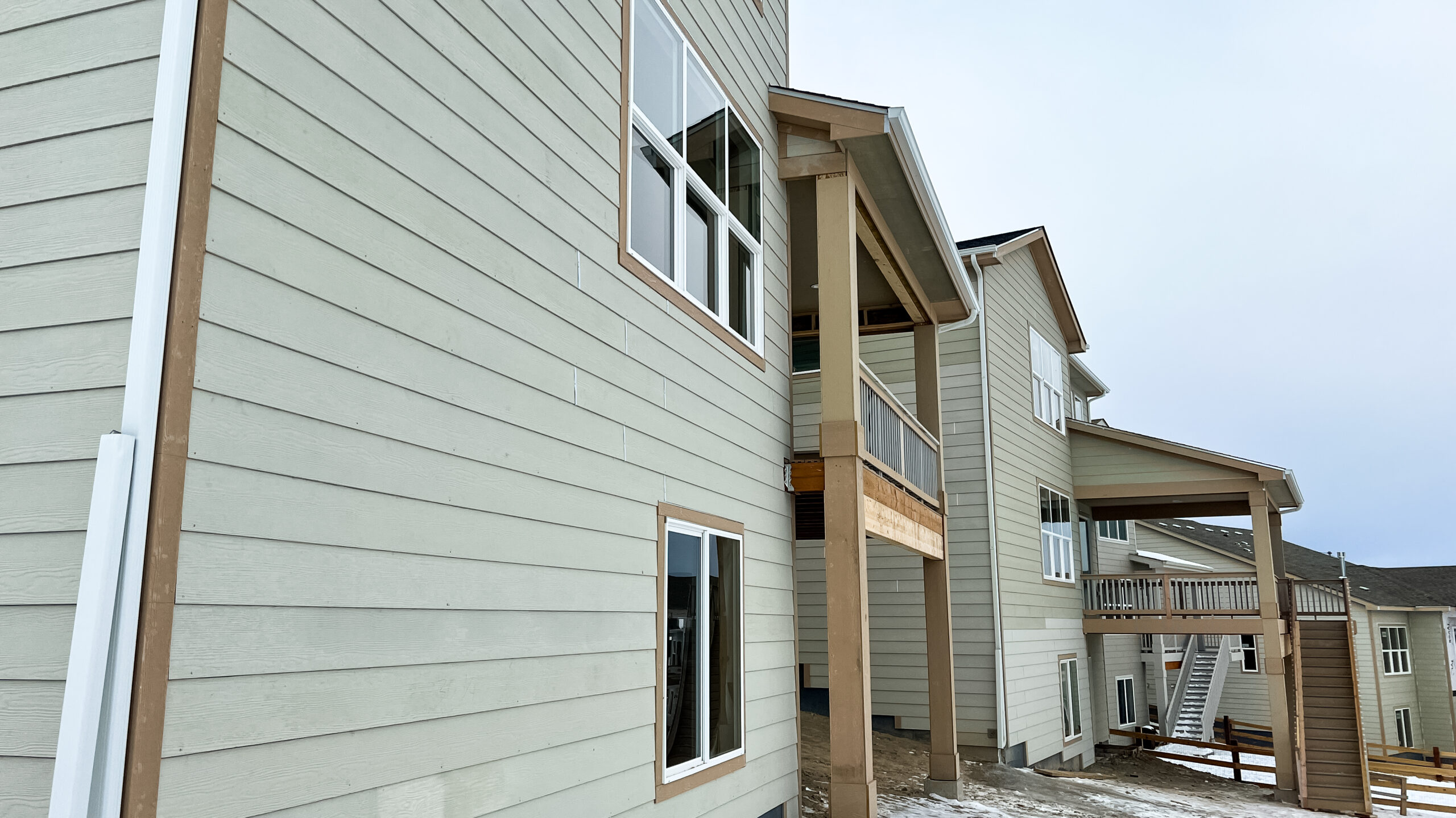 Castle Pines, Colorado USA - January 18, 2023-A view of the rear exterior of multiple new residential homes under construction in a suburban neighborhood. The homes feature modern siding, large windows, and elevated decks. The unfinished yards and snow-covered ground emphasize the ongoing development.
