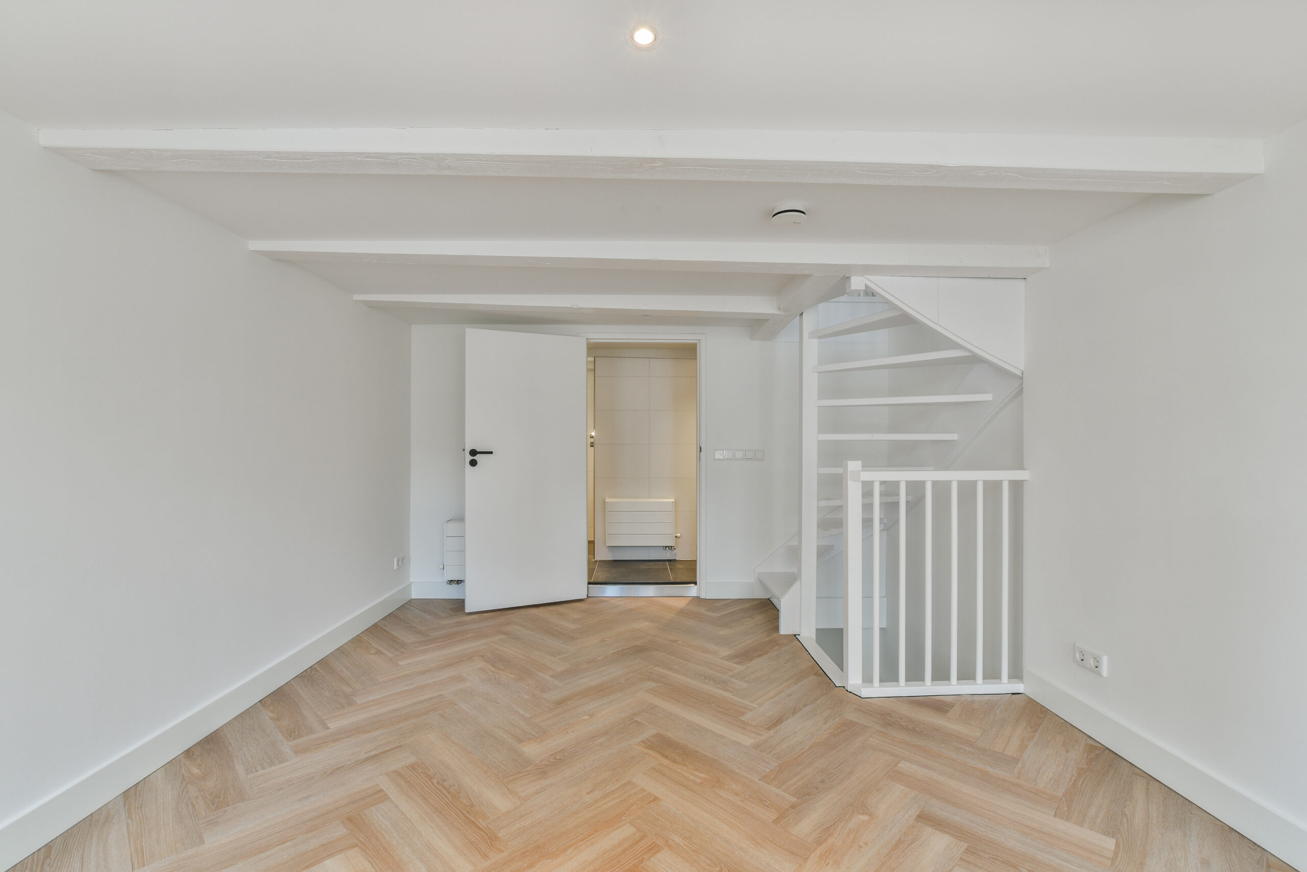 an empty room with white walls and wood flooring on one side, there is a staircase leading up to the second floor