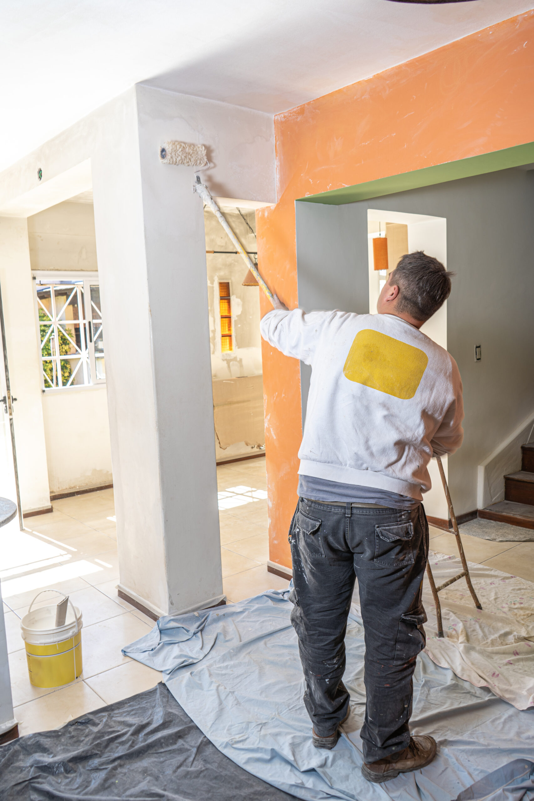 Young man painted with a roller a wall with white color. Concept of specialized work, trade.